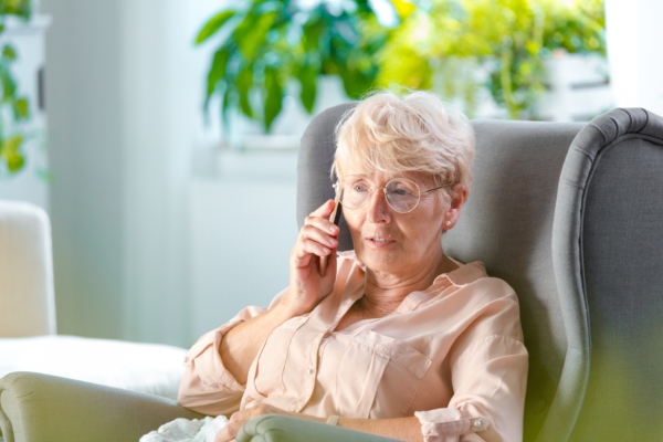 Ältere Frau im Lehnstuhl telefoniert am Handy
